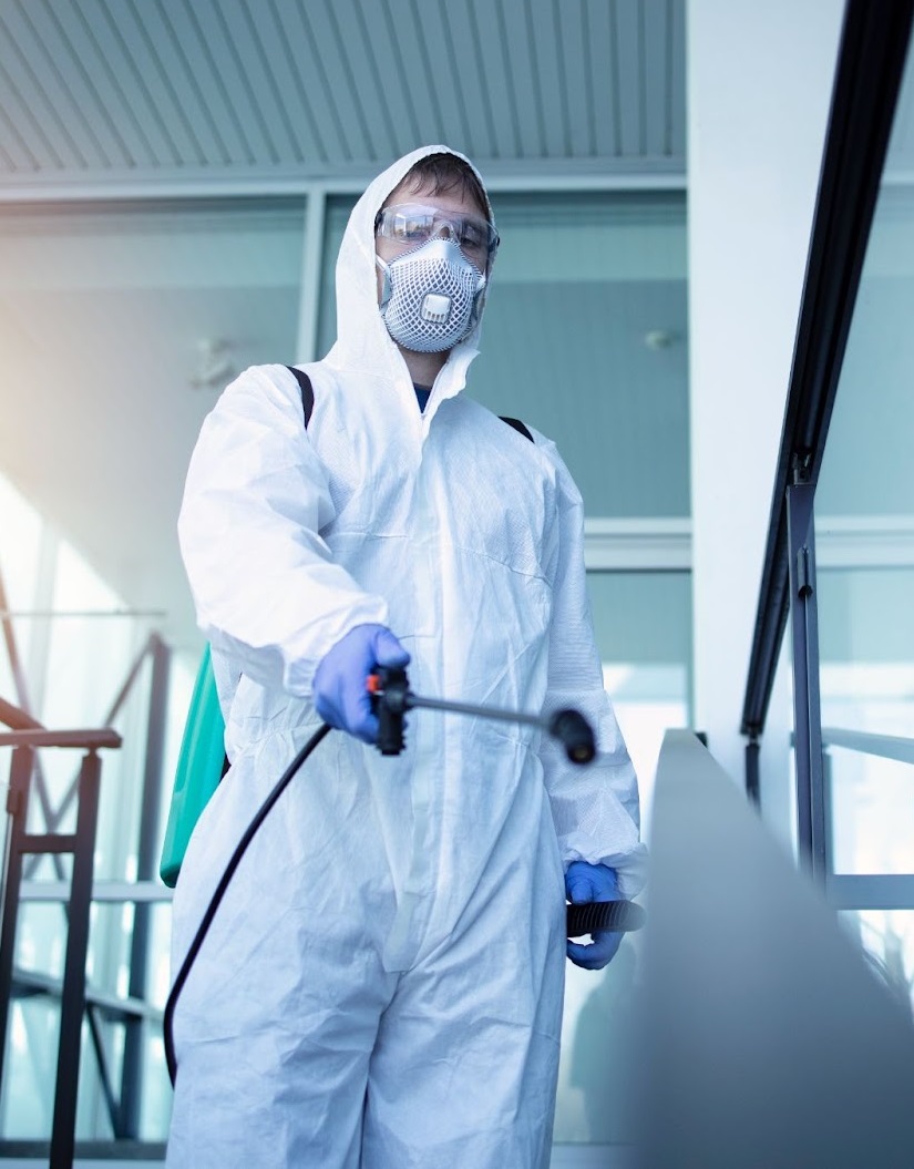 Profissional com macacão, máscara e luvas aplicando produto
